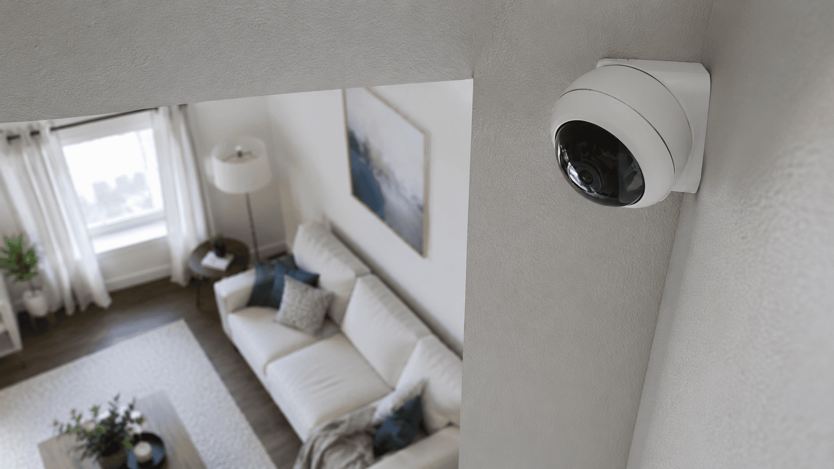 Overhead view of a home security camera mounted in a corner of a living room, empty room below