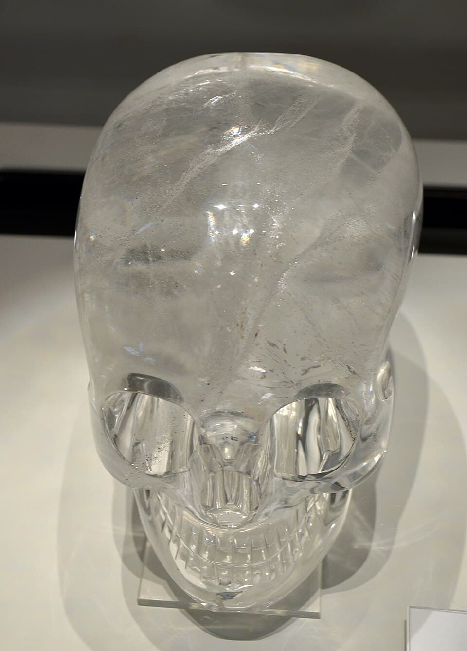 A life-size human skull carved from clear quartz, seen from the front in a museum case
