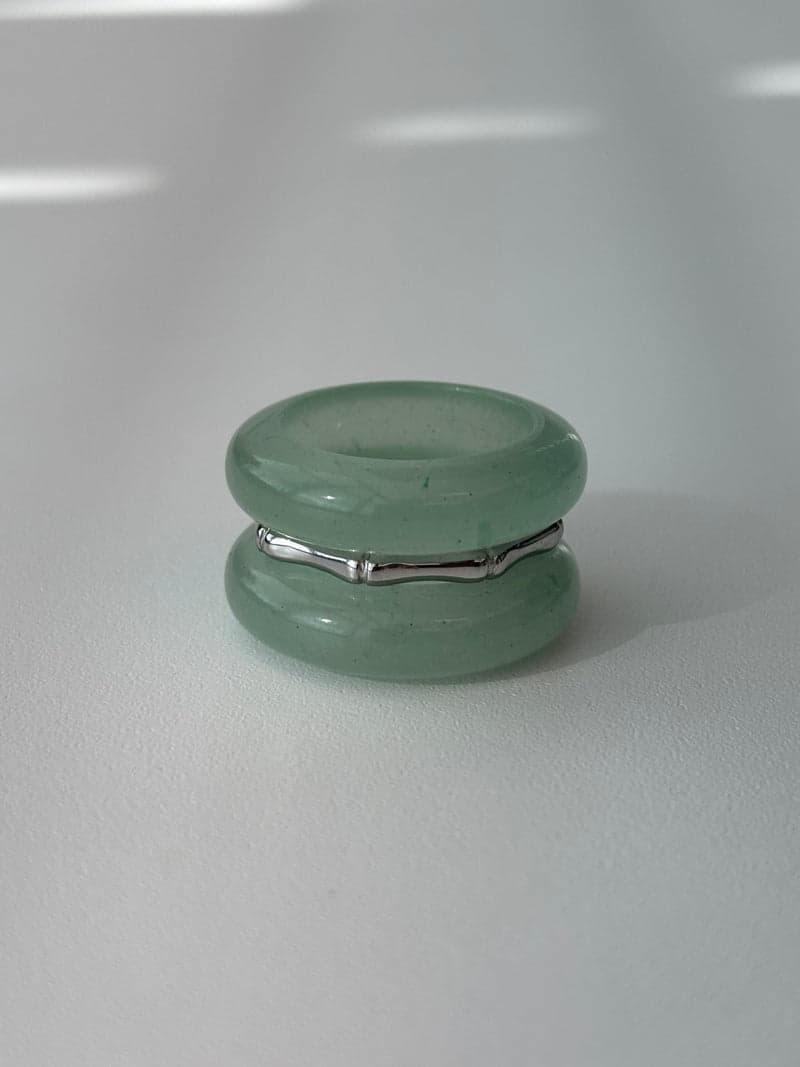 Two pale green stone band rings stacked with a thin silver bamboo-shaped ring between them, on a white surface in window light