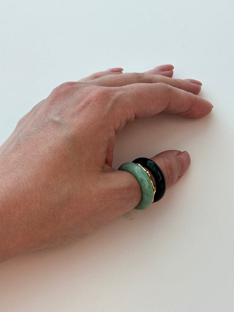 A hand resting on a white surface wearing the dark and pale green stone rings stacked on one finger