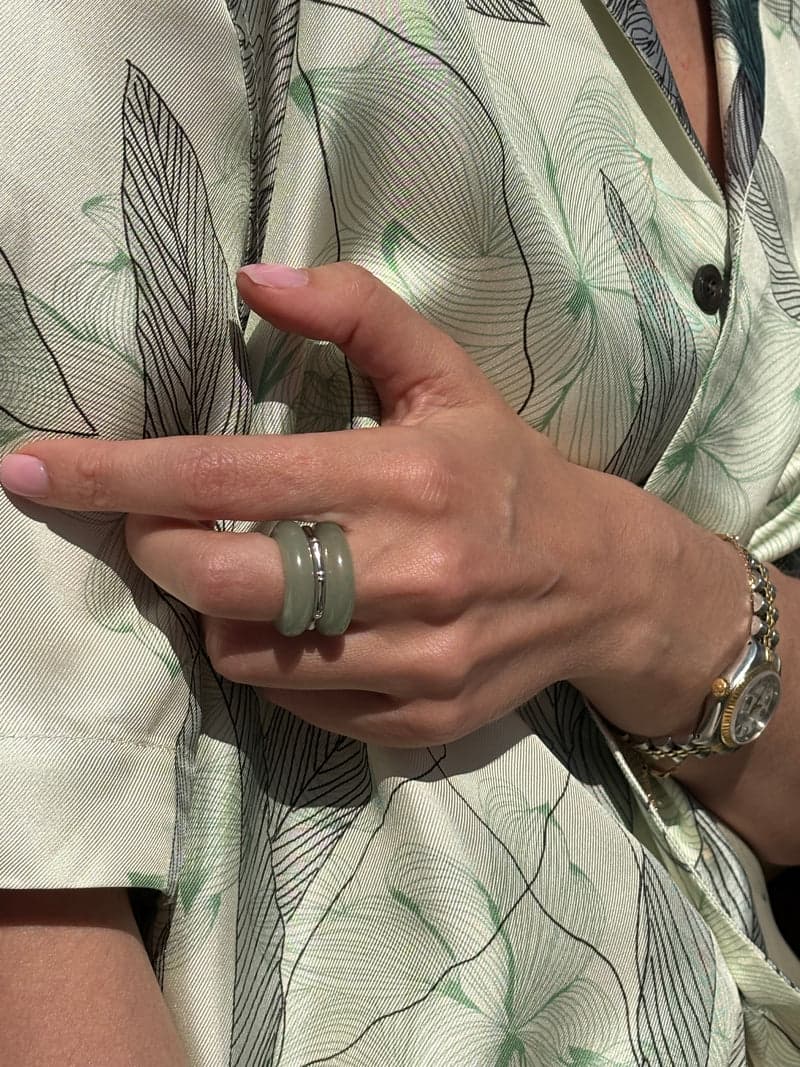A hand resting against a pale printed silk shirt, wearing the green stone rings stacked on one finger