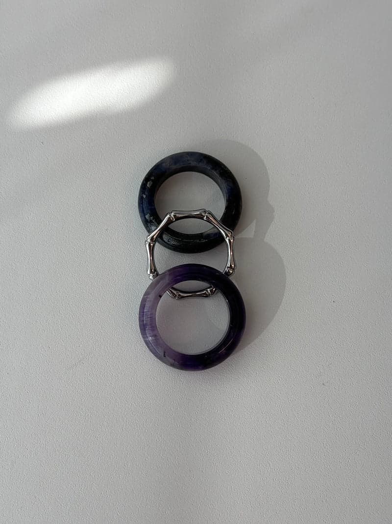 Two stone rings and a thin silver-toned bamboo-shaped ring laid in a vertical line: a dark blue band, the silver ring and a purple band