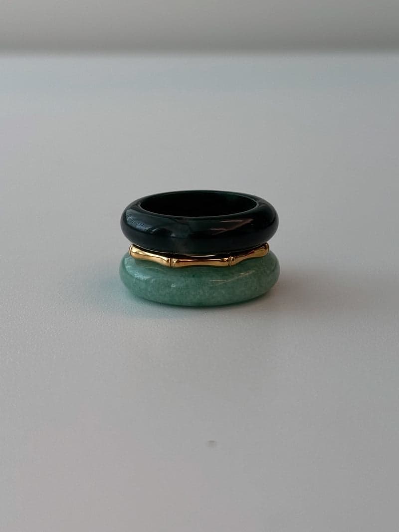 A stacked ring set: a very dark green stone band on top, a thin gold bamboo-shaped ring, and a pale green stone band below