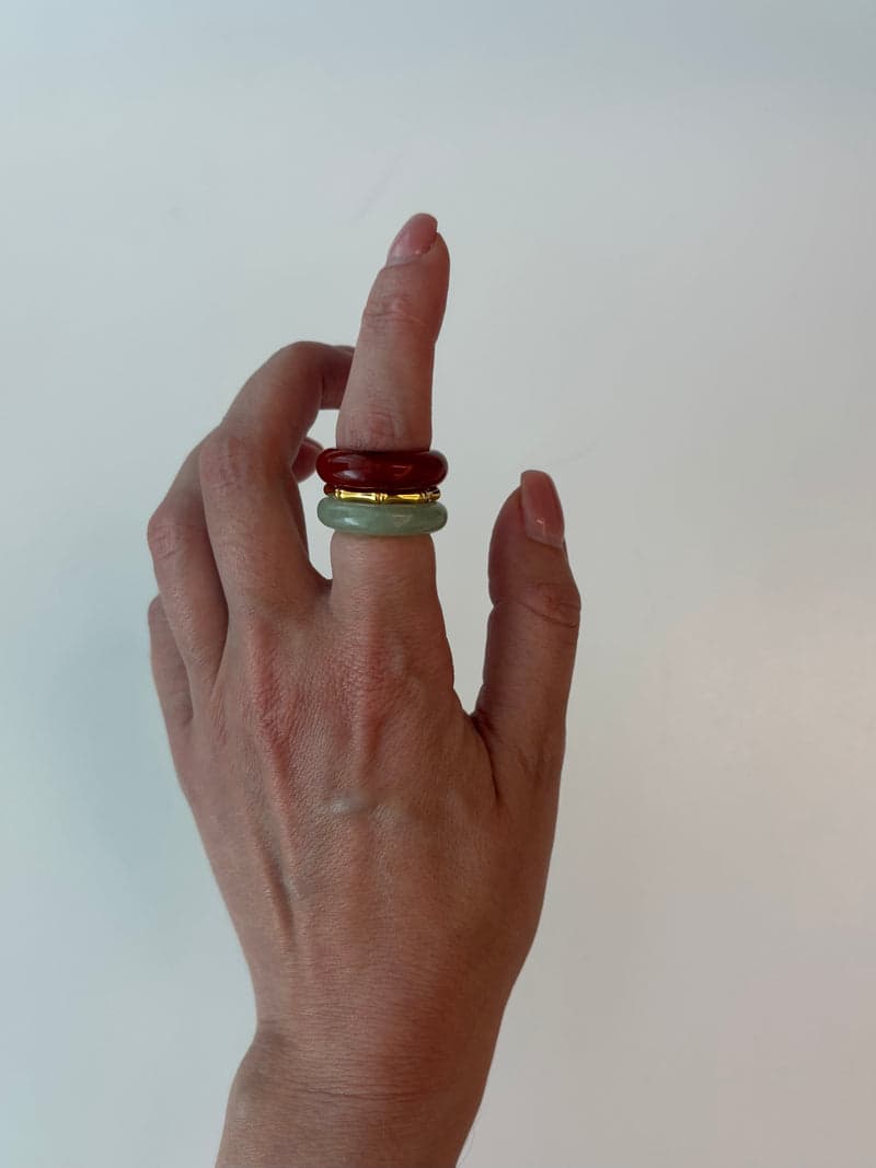 A raised hand wearing the red and pale green stone rings stacked on one finger