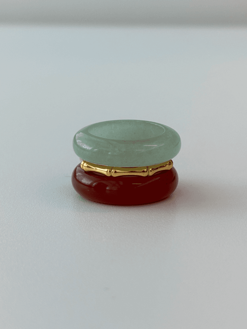 A stacked ring set: a pale green stone band on top, a thin gold bamboo-shaped ring, and a deep red stone band below