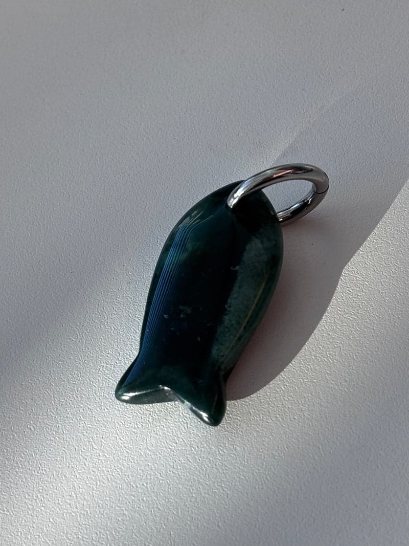 A small carved fish pendant in very dark green stone with a silver ring, on a white surface in window light