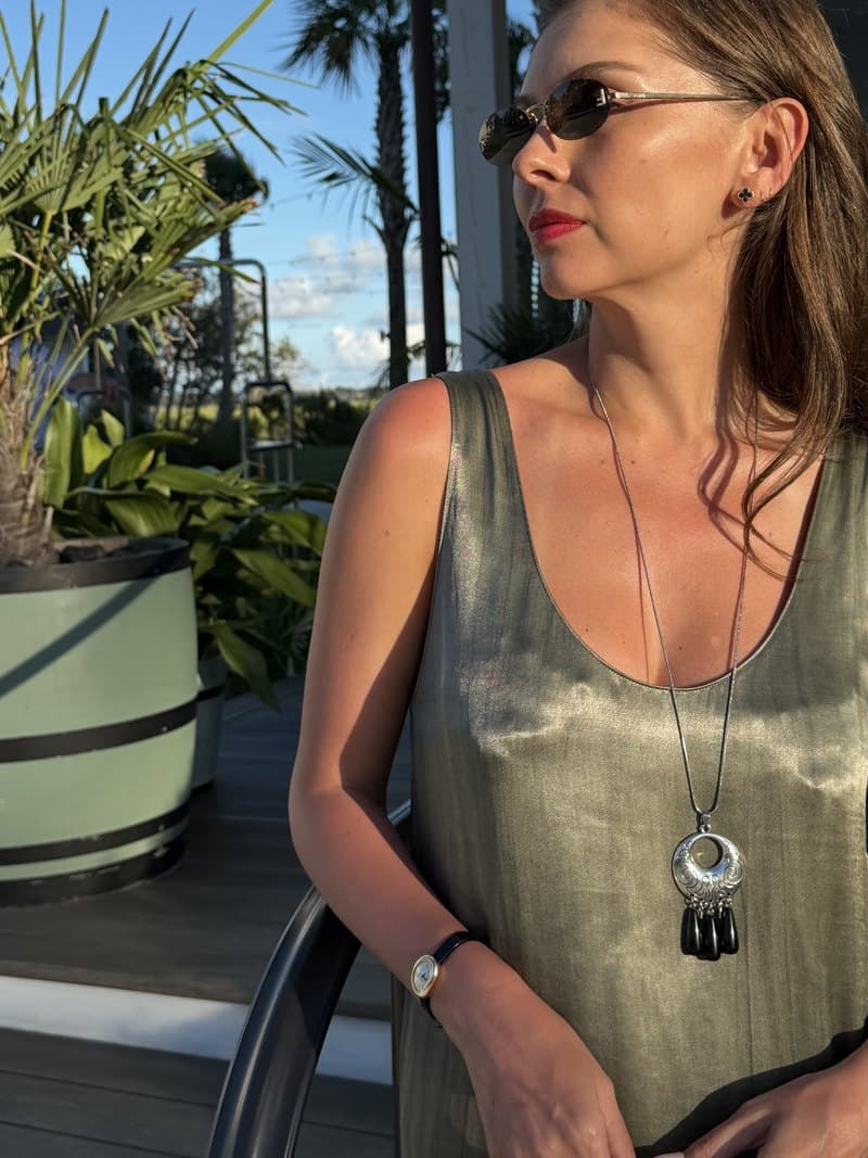 The three teardrop obsidian pendant worn on a long silver chain over a gold dress, outdoors in late afternoon sun