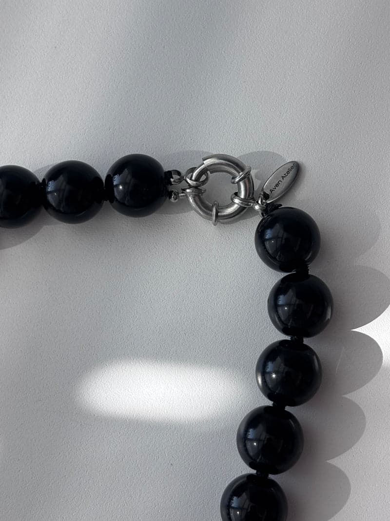 A close view of large glossy black beads beside a silver clasp, on a white surface in window light