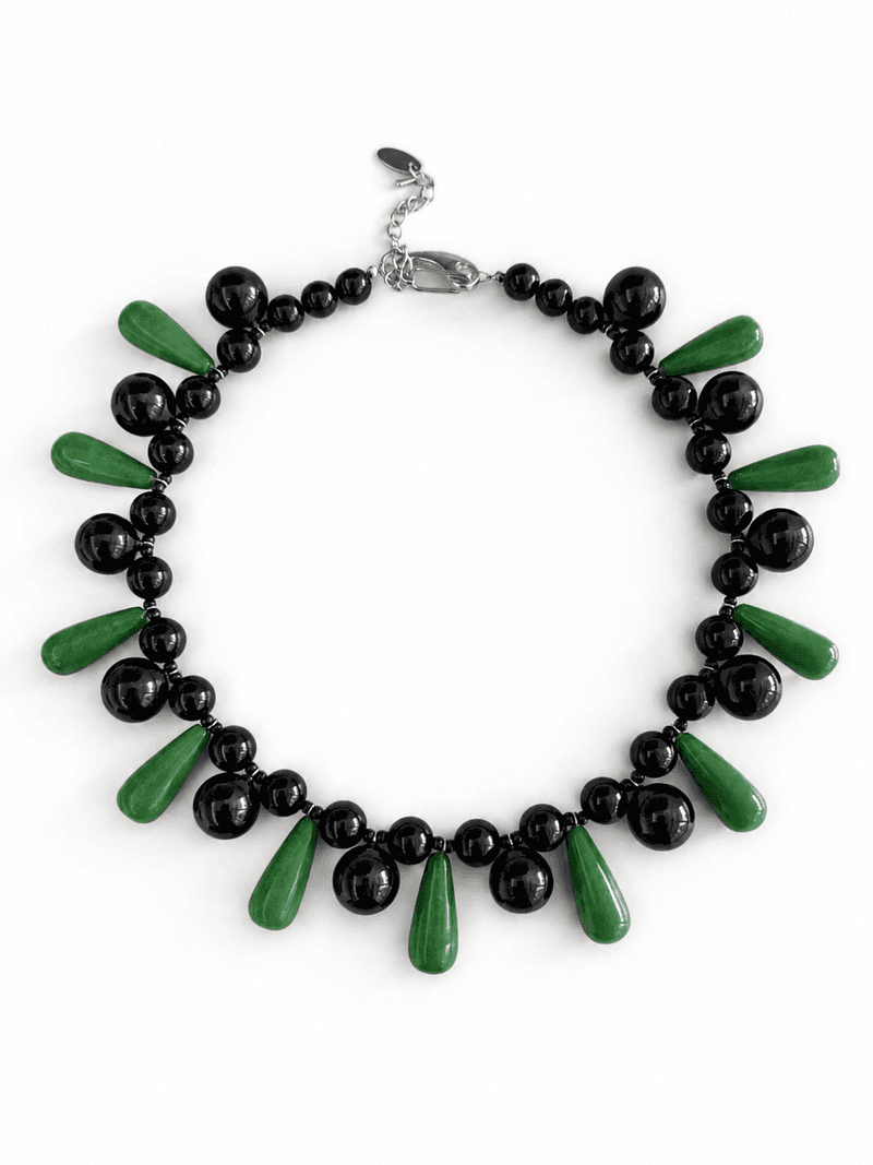 A bib necklace of round glossy black beads alternating with long green teardrop beads, on a white background