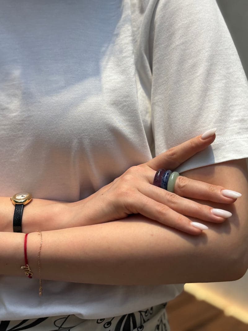 A woman in a white t-shirt with arms folded, wearing the green, blue and purple stone rings stacked on one finger