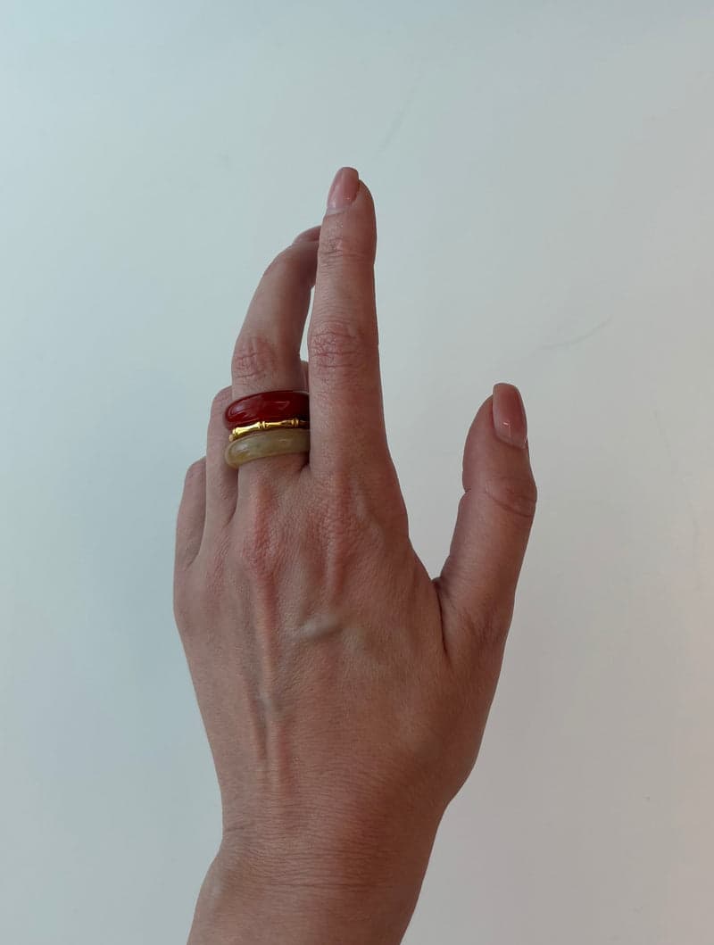 A raised hand wearing the red and pale yellow stone rings stacked on one finger