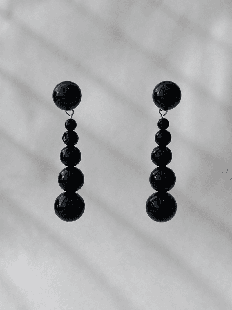 A pair of drop earrings, each a line of glossy black beads graduating from small to large