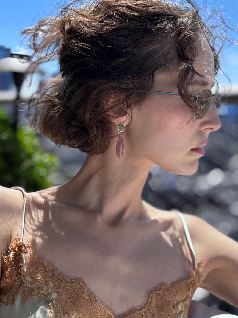 A woman in profile in bright sun on a rooftop wearing a green and pink drop earring