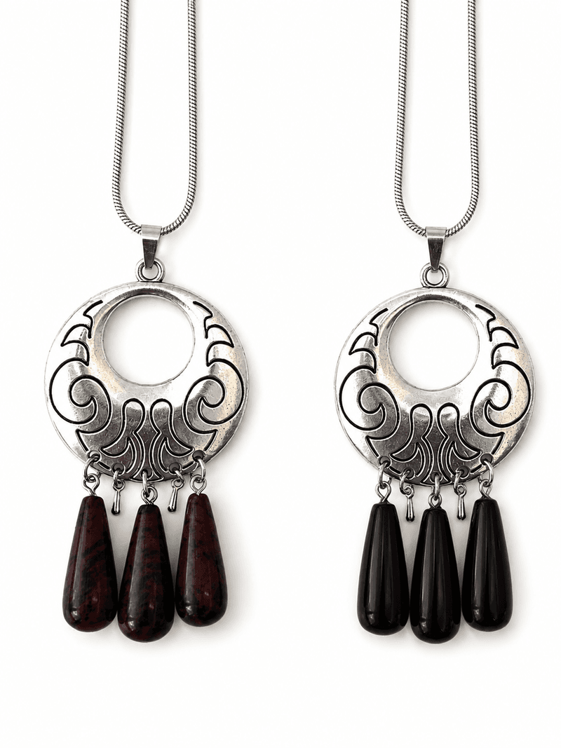 Two versions of the same silver filigree pendant necklace side by side, one with dark red teardrops and one with black teardrops