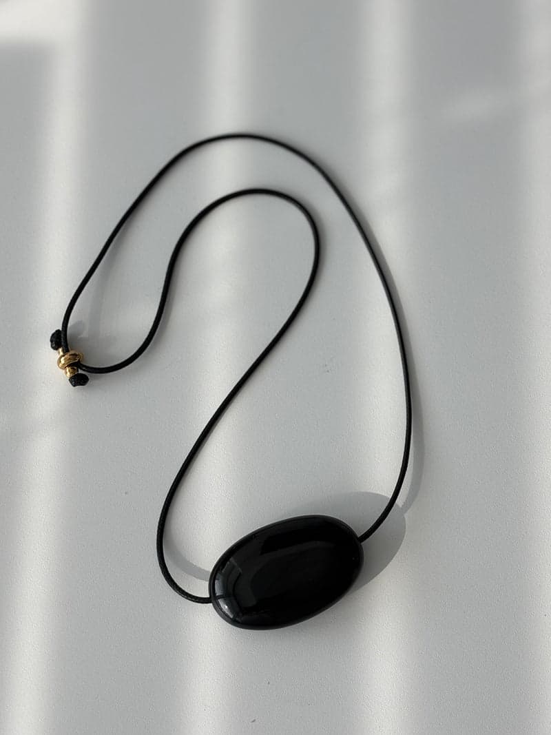 A single polished black obsidian pendant on a black cord, laid flat