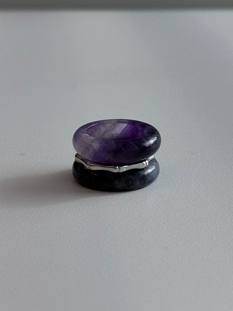 A stacked ring set: a purple stone band on top, a thin silver bamboo-shaped ring, and a dark blue stone band below