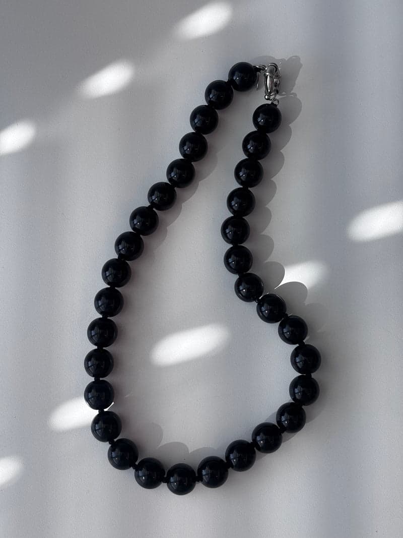 A strand of large round glossy black beads laid in a curve on a white surface in window light