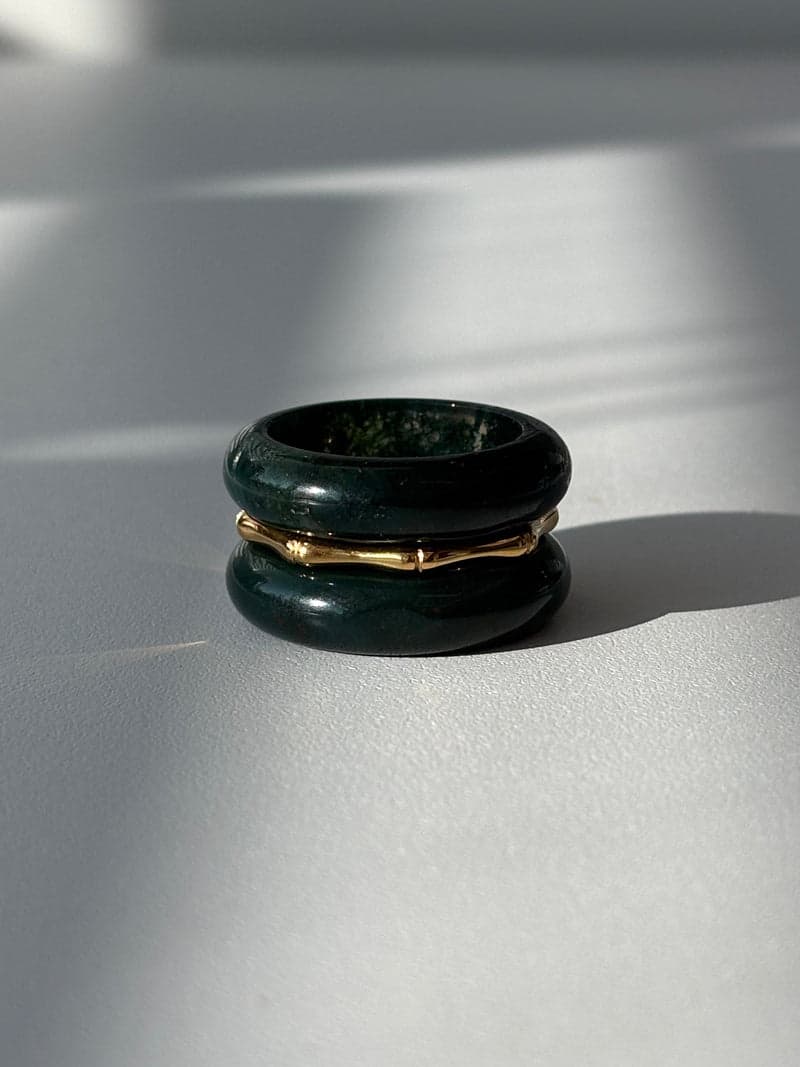 Two deep green stone band rings stacked with a thin gold bamboo-shaped ring between them, in window light