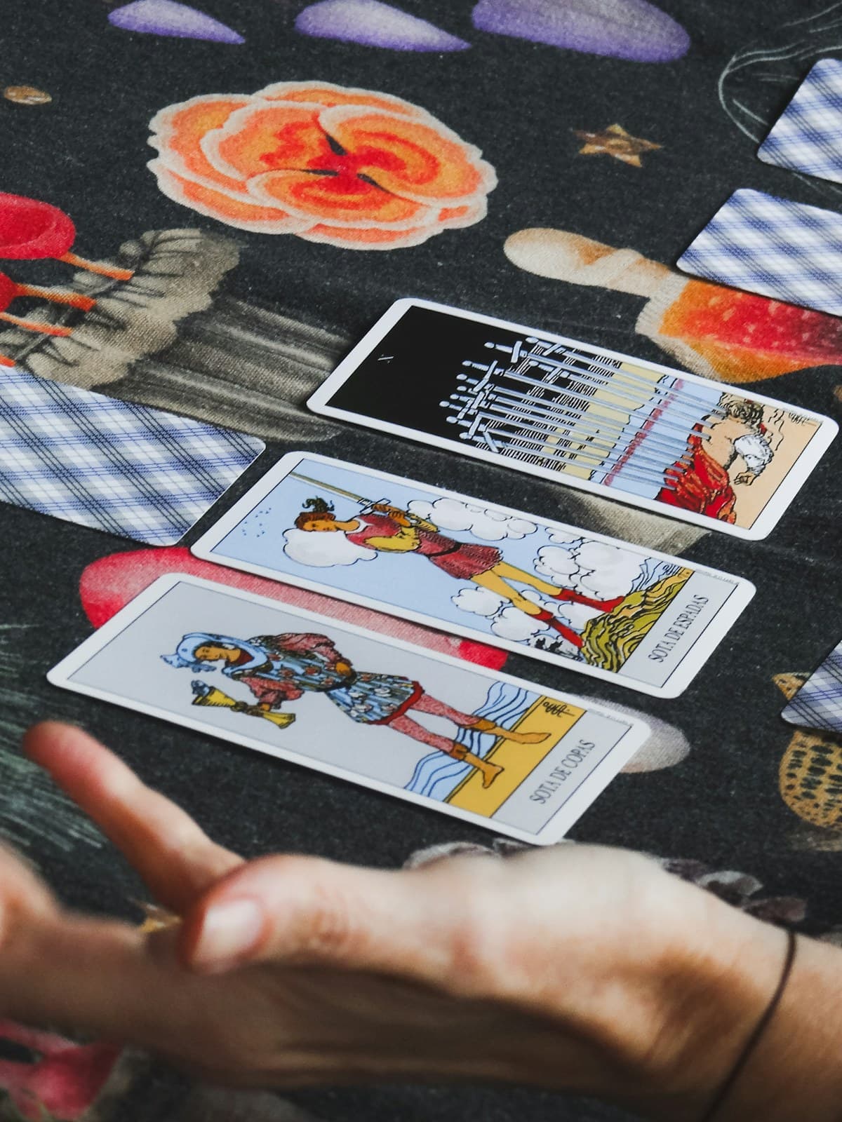 Manos colocando cartas de tarot sobre una tela oscura estampada