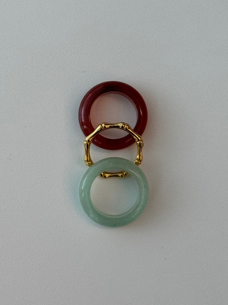Two stone rings and a thin gold bamboo-shaped ring laid in a vertical line: a deep red band, the gold ring and a pale green band