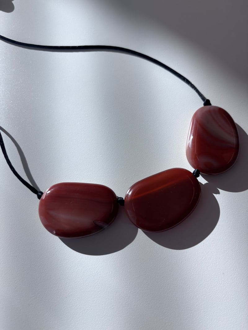 Three large flat oval stones in translucent red brown with paler curved bands, strung on a black cord