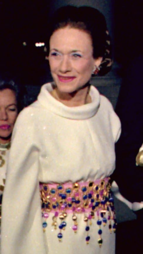 The Duchess of Windsor smiling, wearing a white high-necked top, at an evening reception