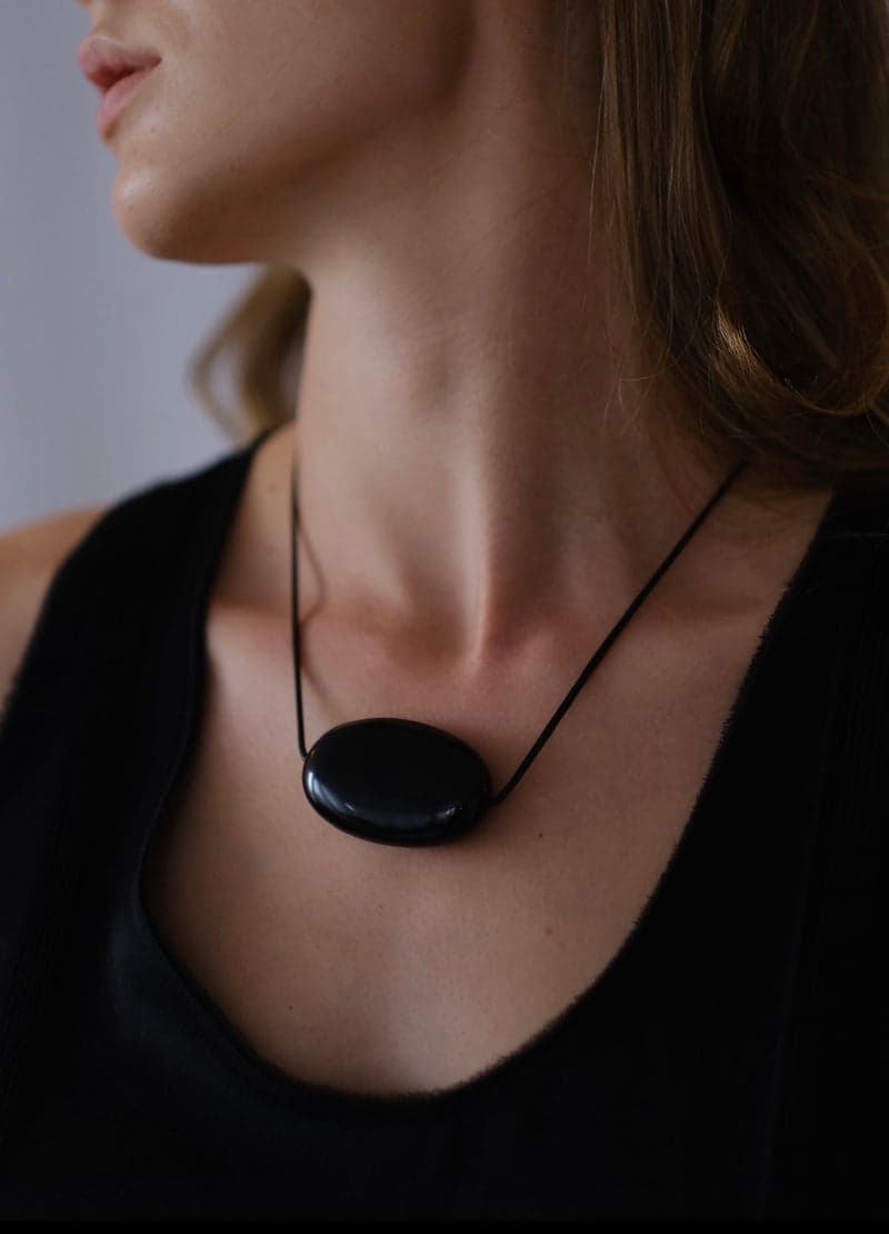 The same black obsidian pendant worn at the collarbone on a fine black cord