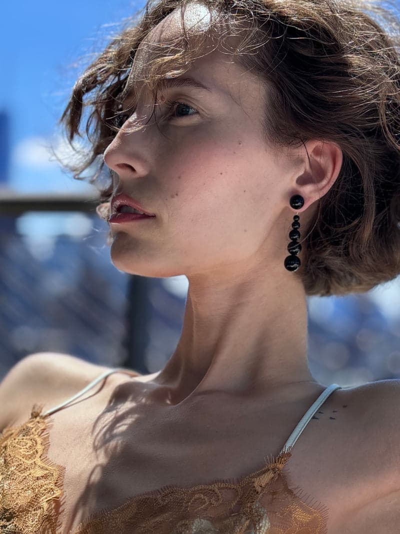A woman in profile in bright sun wearing a black beaded drop earring