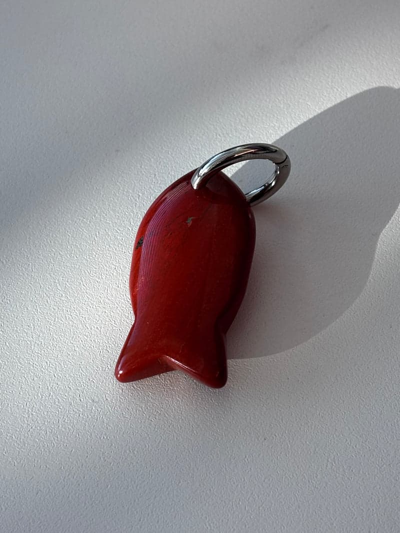A small carved fish pendant in glossy deep red stone with a silver ring, on a white surface in window light