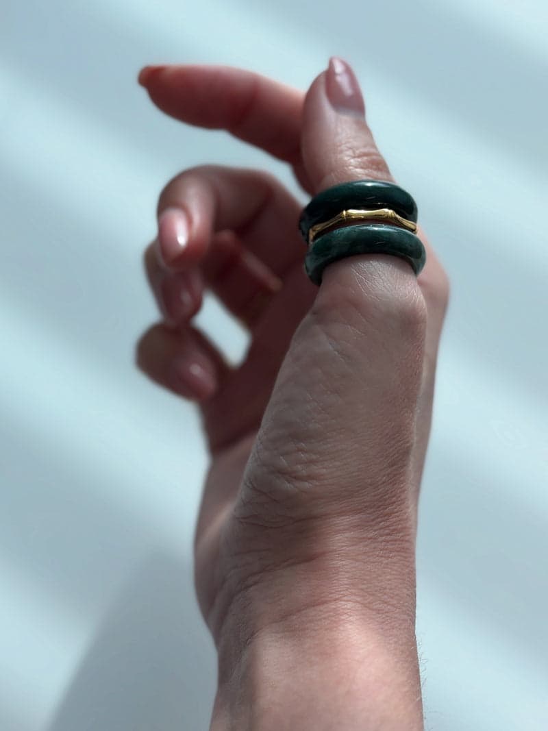 A raised hand in window light wearing the deep green stone rings stacked on one finger
