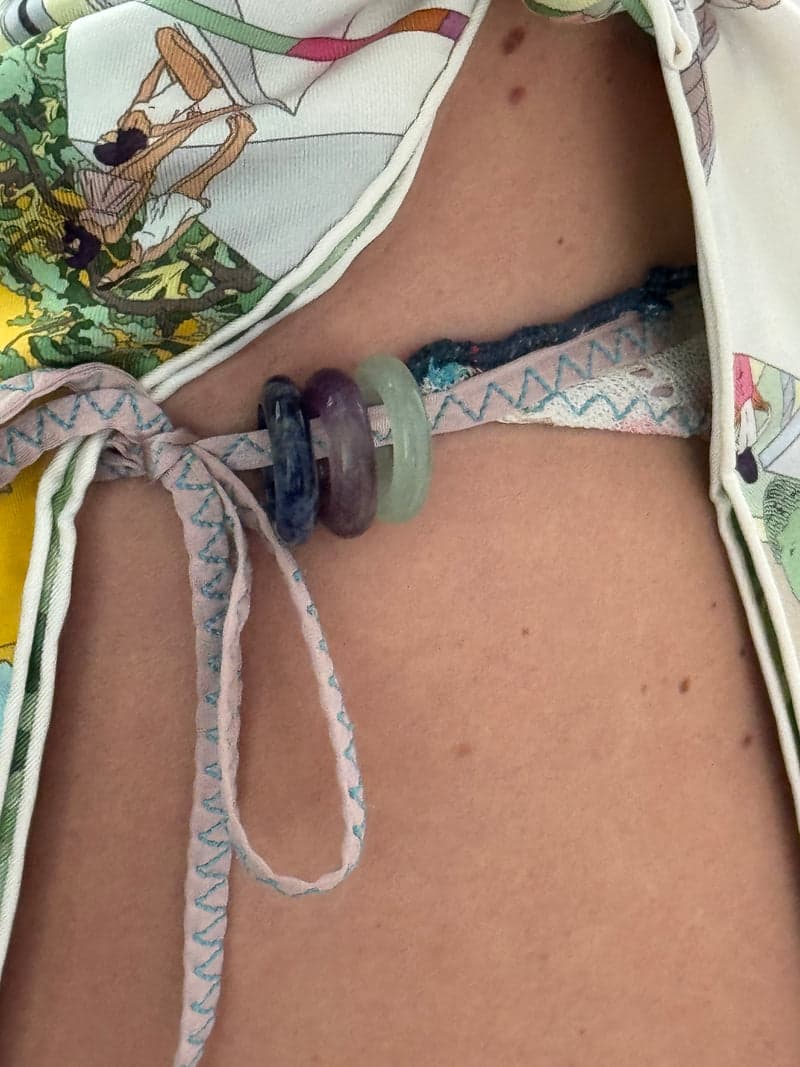 The blue, purple and green stone rings threaded onto the tie of a patterned bikini at the hip
