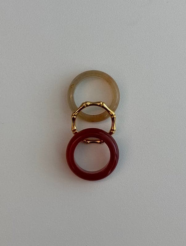 Two stone rings and a thin gold bamboo-shaped ring laid in a vertical line: a pale yellow band, the gold ring, and a deep red band