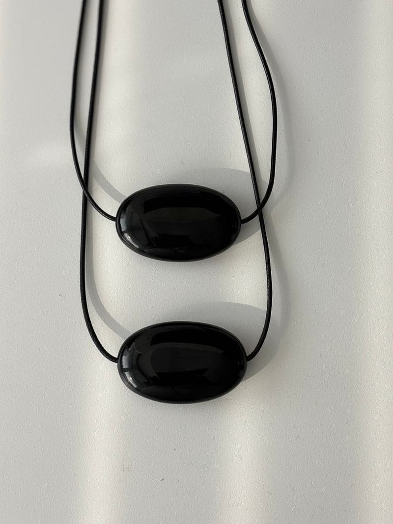 Two polished black obsidian bean pendants on cords, seen from above