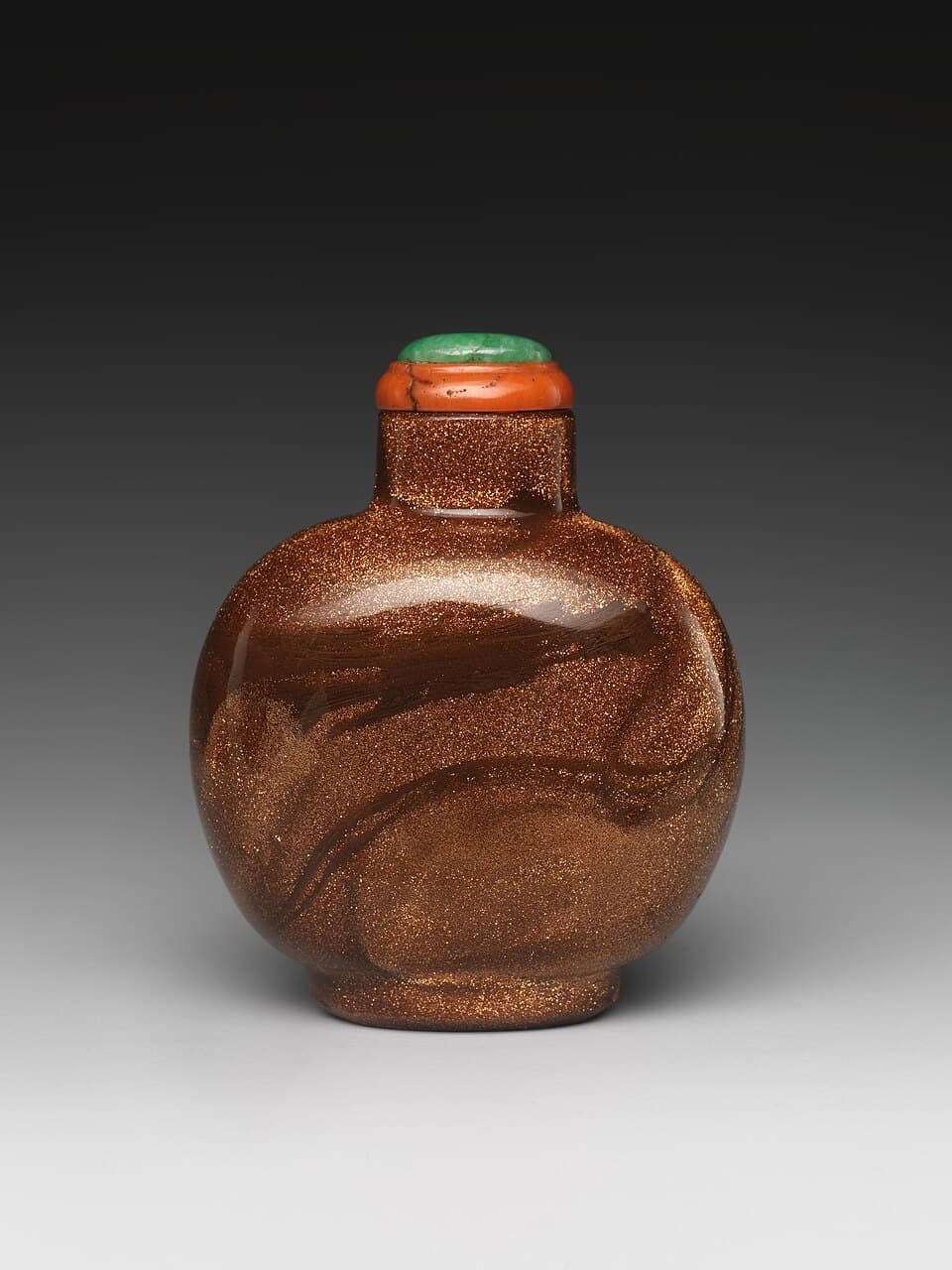 A small round brown glass snuff bottle full of fine copper sparkles, with a stopper, on a grey background