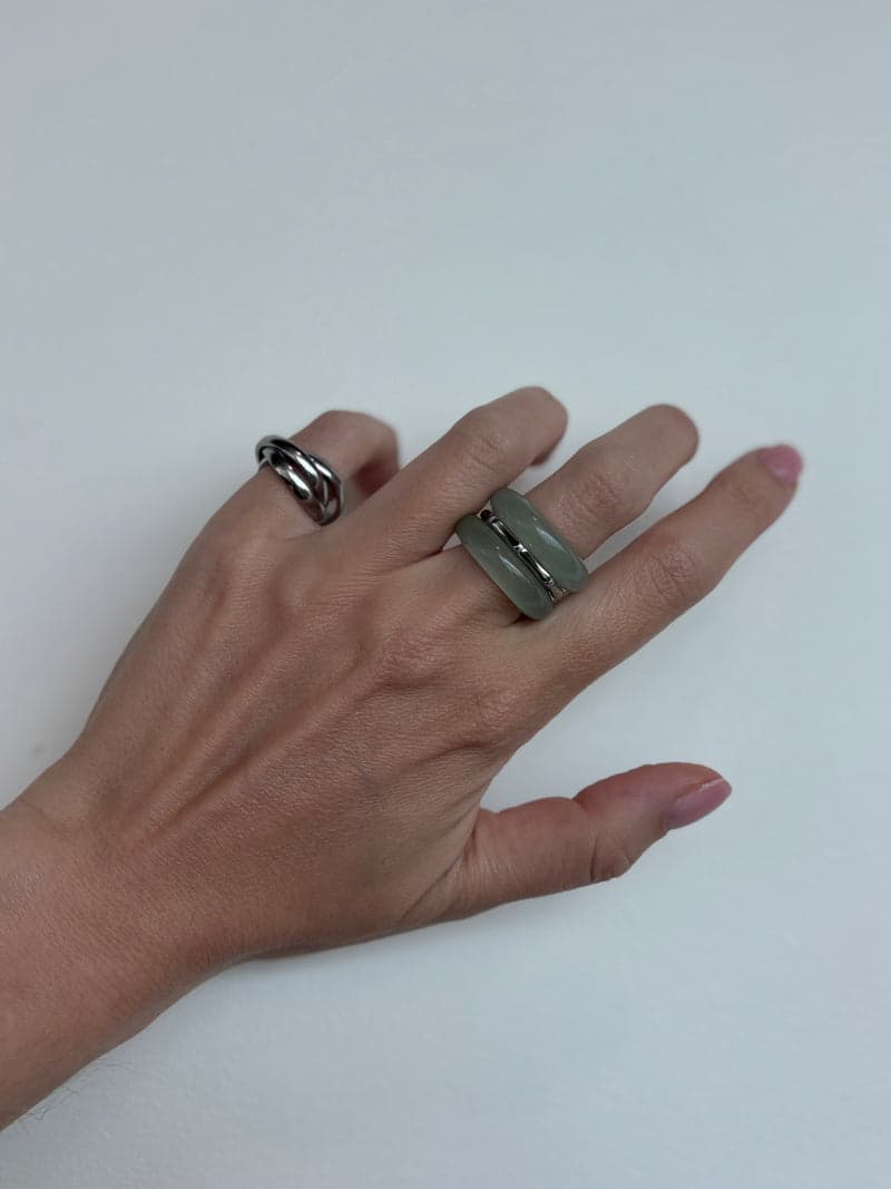 A hand resting flat on a white surface wearing the pale green stone rings and a silver ring