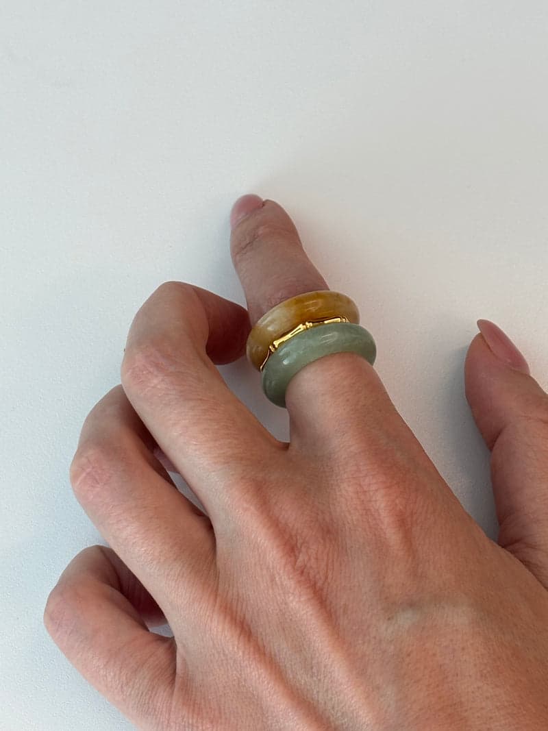 A hand resting on a white surface wearing the orange and pale green stone rings stacked on one finger