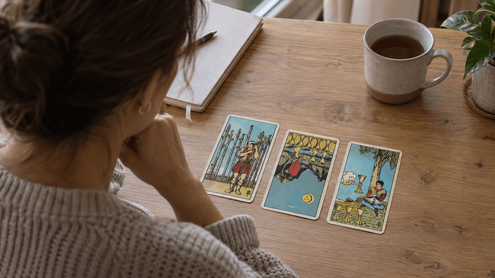 A tarot reader comparing one reversed card with two upright cards in a three-card spread on a wooden table.