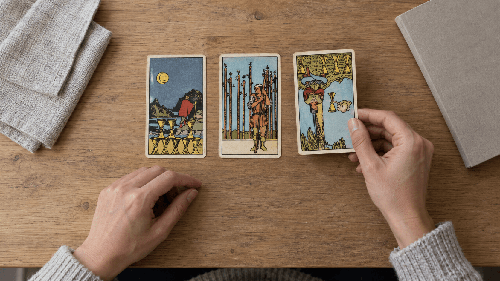 Overhead view of a reader placing the third card in a yes-or-no tarot spread with two upright cards and one reversed card.